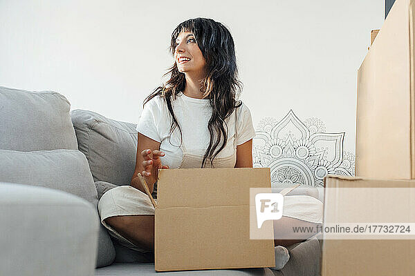Woman with cardboard box sitting on sofa in living room at home