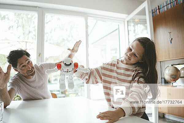 Girl playing with toy robot by father sitting at table