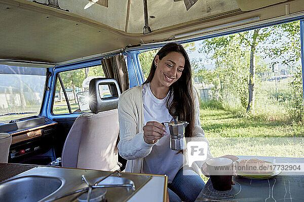 Lächelnde Frau hält Kaffeekanne neben Tasse im Wohnmobil