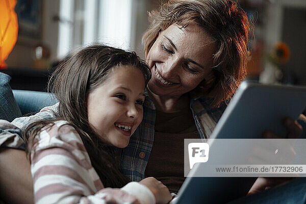 Glückliche Mutter und Tochter sitzen zu Hause mit Tablet-PC