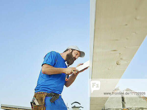 Worker sawing wood with handsaw at construction site