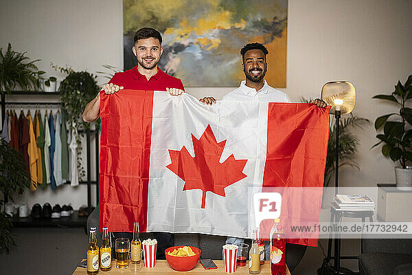 Happy young men standing with Canadian flag at home