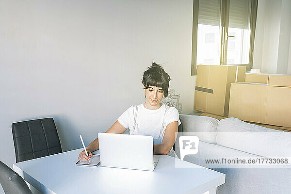 Woman with digitized pen using tablet PC looking at laptop on table in living room