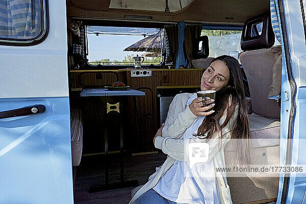 Frau mit Kaffeetasse träumt vor der Tür des Wohnmobils