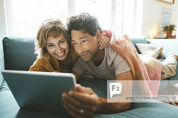 Happy mature couple using tablet PC lying on sofa at home