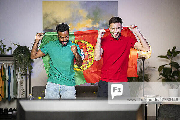 Happy young men with Portuguese flag enjoying football match at home
