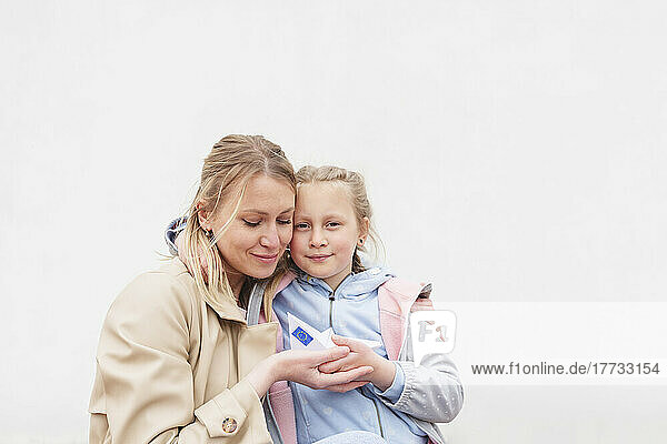 Mother and daughter holding paper boat with European Union Flag against white background
