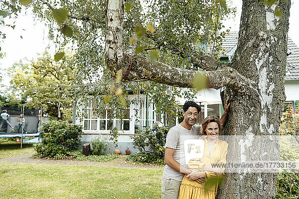 Happy couple standing by tree in front of house