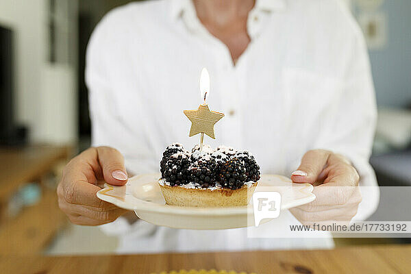 Woman holding plate of blackberry tart with lit candle at home