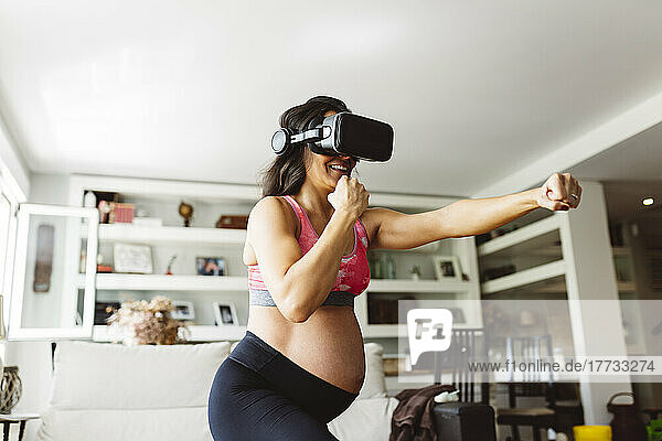 Happy pregnant woman wearing virtual reality simulator punching at home