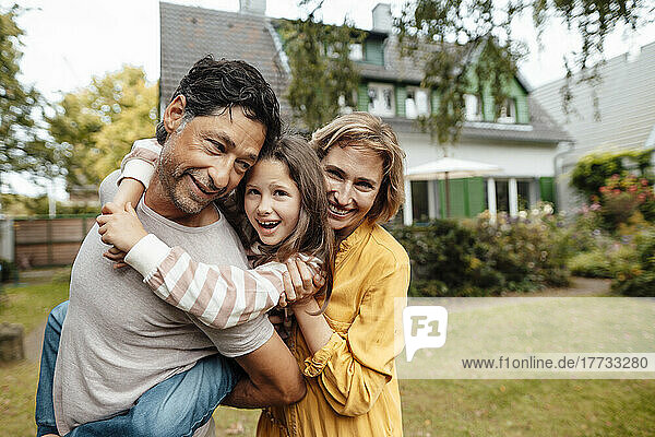 Smiling man giving piggyback ride to daughter by woman in front of house