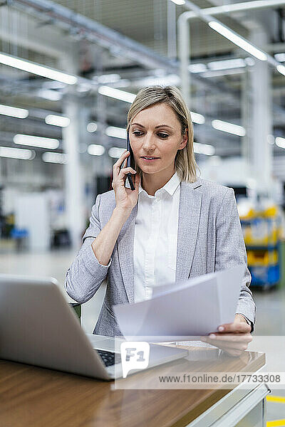Businesswoman with laptop on the phone in factory