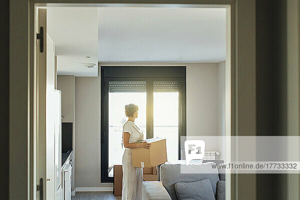 Frau mit Karton steht im Wohnzimmer im neuen Zuhause