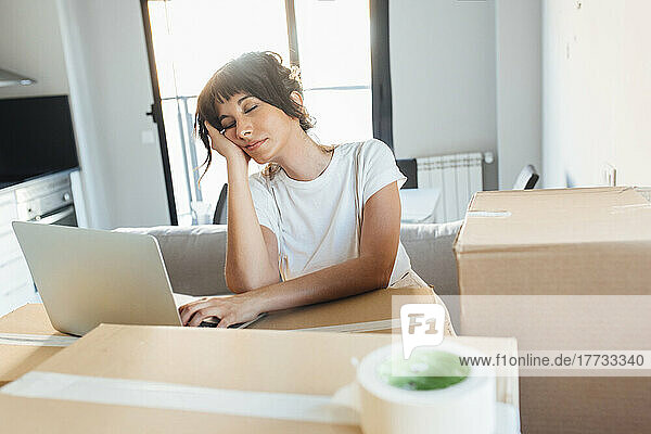 Tired woman with laptop on cardboard at new home
