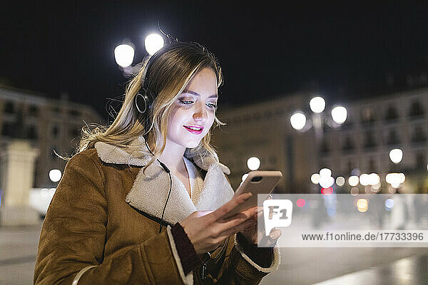 Frau mit Smartphone hört Musik über Kopfhörer in der Stadt