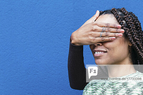 Hand of woman covering eyes of friend in front of blue wall