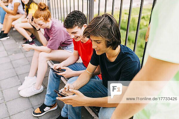 Boy using smart phone sitting by friends