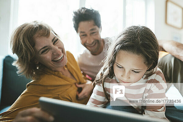 Happy parents looking at daughter using tablet PC
