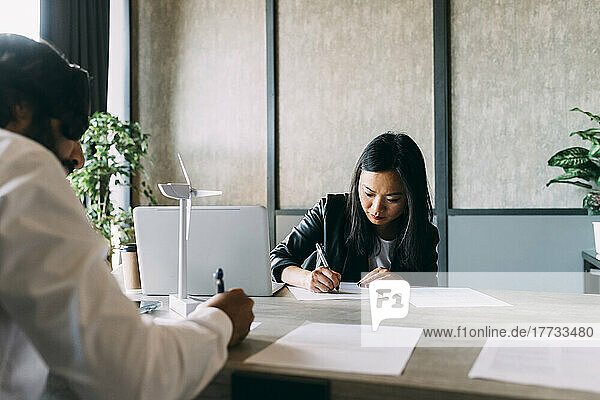 Business colleagues writing on paper document at desk in office