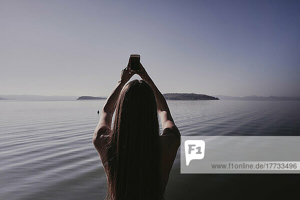 Frau fotografiert mit Handy am See