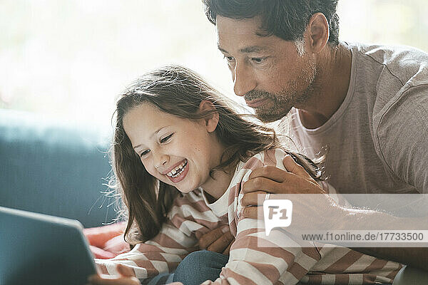 Mature man with cheerful daughter using digital tablet at home
