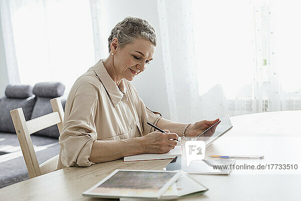 Woman using digital tablet and taking notes at table at home