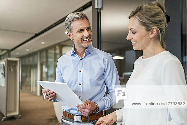 Smiling businessman with digital tablet and businesswoman talking in office