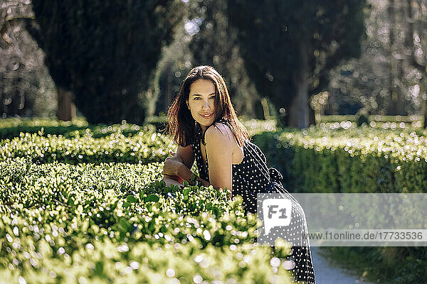 Smiling beautiful woman leaning on hedge in garden