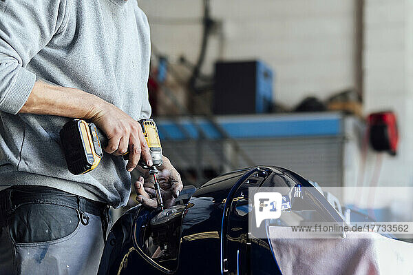 Hands of mechanic repairing vehicle part with electric screwdriver at workshop