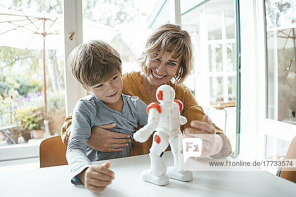 Glückliche Mutter und Sohn spielen zu Hause mit Spielzeugroboter
