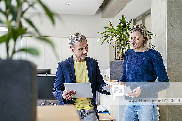 Businessman and businesswoman working together on digital tablet and papers in office