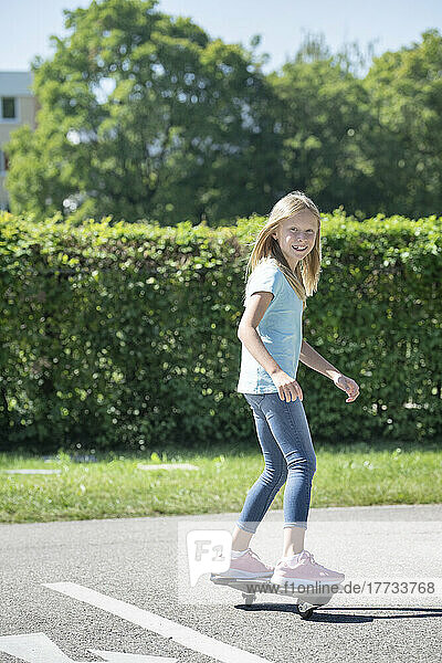Smiling blond girl skateboarding on traffic course