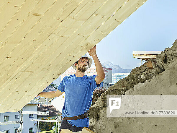 Junger Mann arbeitet auf der Baustelle auf dem Dach eines Hauses