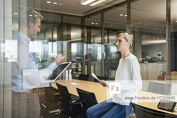 Geschäftsmann und Geschäftsfrau mit digitalem Tablet und Dokumenten unterhalten sich im Büro