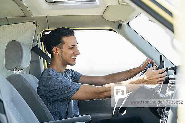 Smiling handsome man using smart phone sitting in van