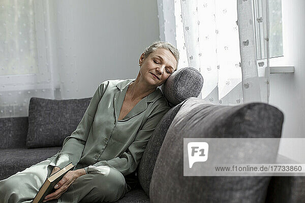 Relaxed mature woman sitting on couch in living room with closed eyes