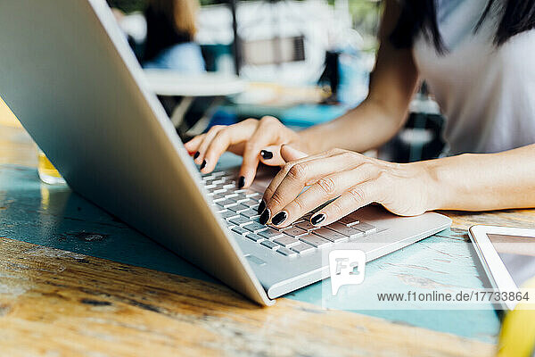 Hands of freelancer typing on laptop at sidewalk cafe