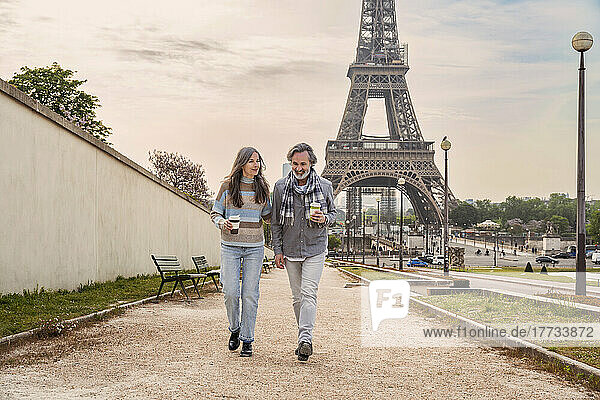 Mature couple with disposable coffee cup walking together in front of Eiffel tower  Paris  France