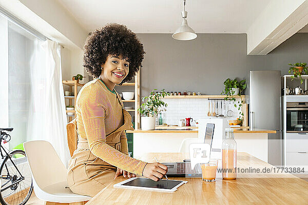 Happy young woman with tablet PC and laptop sitting at table in living room