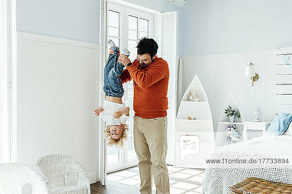 Father holding son upside down standing in bedroom at home