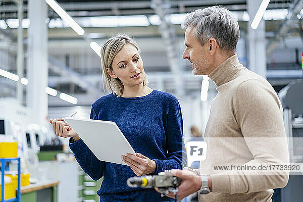 Businessman with device and businesswoman with digital tablet talking in factory