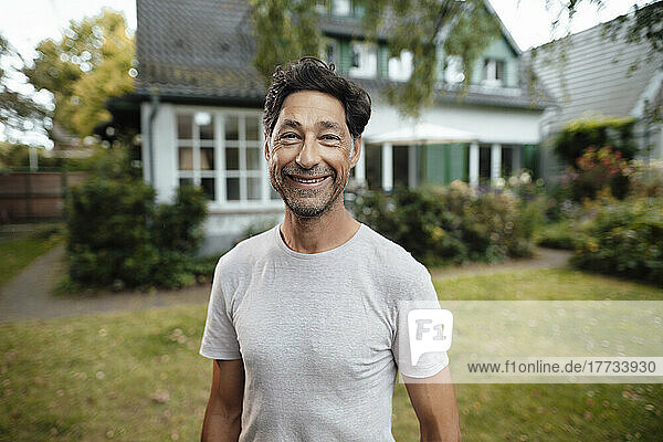 Happy mature man standing in front of house