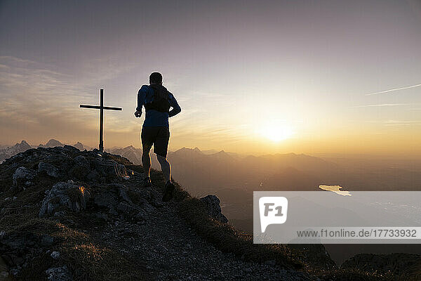 Wanderer läuft auf dem Sauling-Berggipfel mit Gipfelkreuz bei Sonnenuntergang