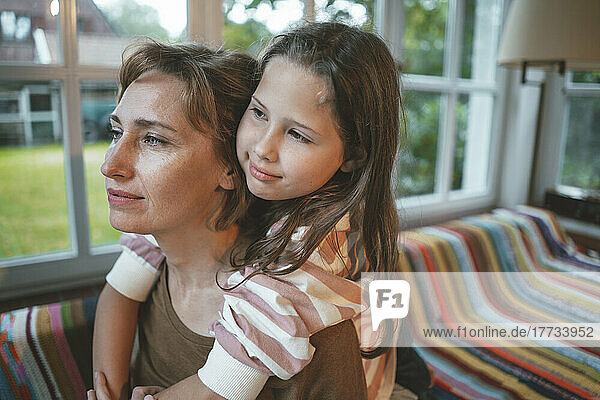 Mother with daughter sitting on sofa in front of window