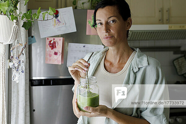 Woman drinking celery smoothie from mason jar at home