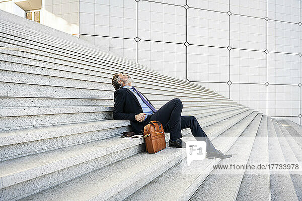 Mature businessman sitting by bag relaxing on steps