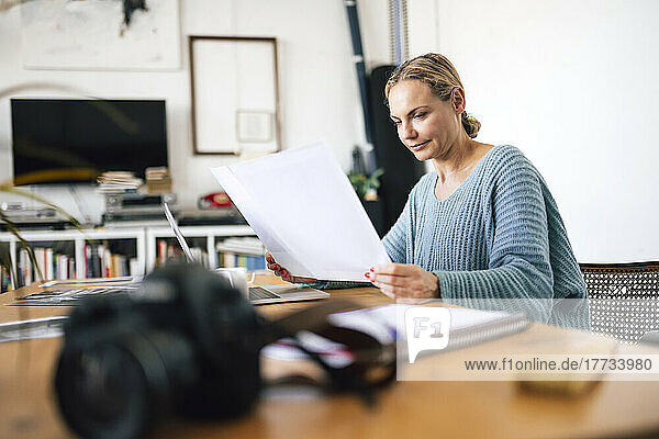 Businesswoman examining photograph sitting with laptop at home
