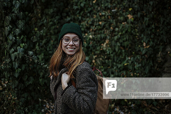 Happy woman wearing knit hat and backpack enjoying at park