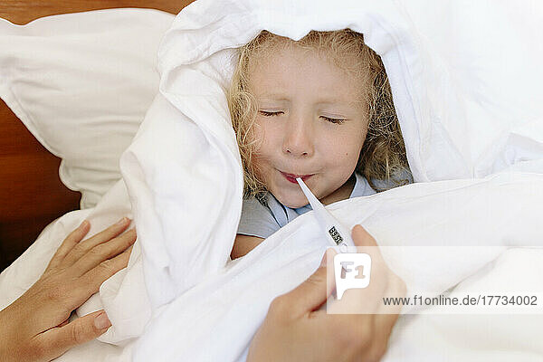 Sick daughter avoiding to use thermometer by mother in bedroom