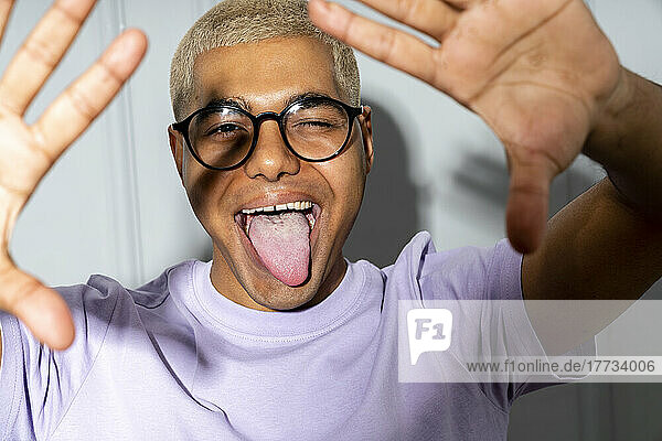 Young man wearing eyeglasses sticking out tongue